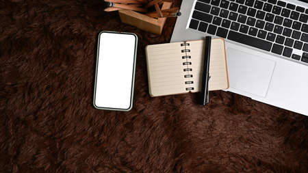 Mock up smart phone with white screen and laptop computer on brown fur rug.