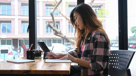 Young asian woman designer sitting near window in office and working with computer tablet.