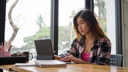 Young asian woman designer sitting near window in office and working with computer tablet.の写真素材