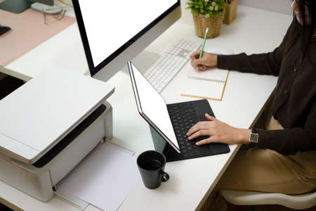 Cropped shot of smiling female graphic designer sitting at her workplace and using mobile phone for...