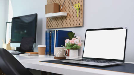 Front view computer laptop with empty screen, coffee cup, pencil holder, notebook and house plant on...