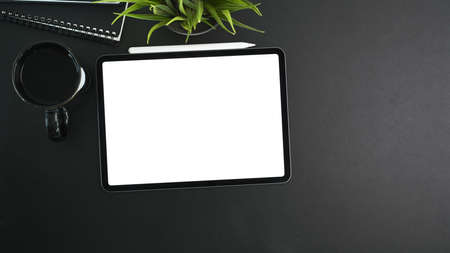 Mock up digital tablet with empty screen, coffee cup, house plant, notebook and copy space on black...