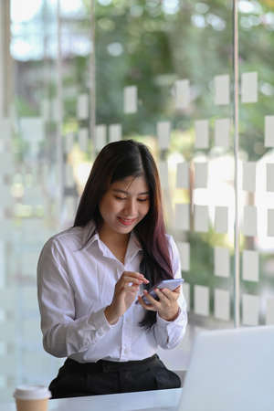 Portrait of happy young woman office worker sitting in office and using mobile phone.