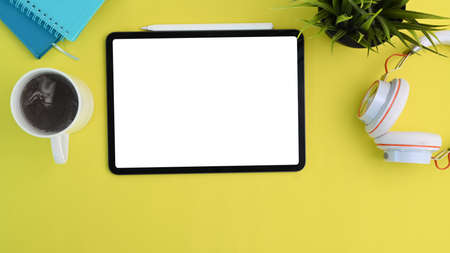 Top view of mock up digital tablet, headphone, coffee cup and plant on yellow background.