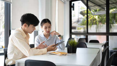 Two young business people analyzing financial report and working with laptop computer in modern...