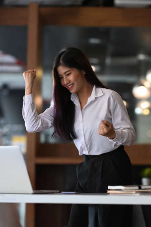 Successful businesswoman looking at laptop computer and raising her arm up to celebrating her success.の写真素材