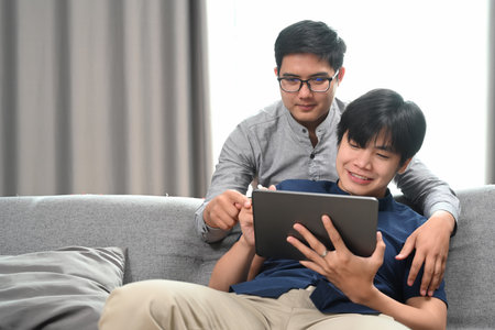 Casual man using digital tablet while sitting with his friend on sofa.の写真素材