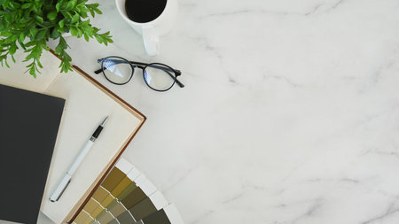 Top view of designer workspace with glasses, coffee cup, notebook, houseplant and color swatch on...