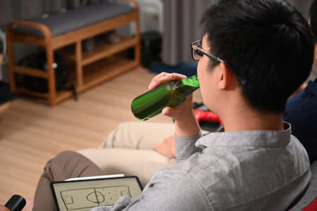 Close up view of casual man holding stylus pen writing on digital tablet while sitting on sofa at home.の写真素材