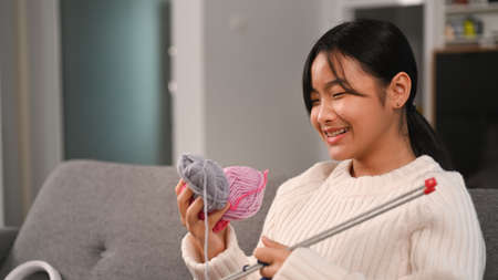 Happy female knitting blue sweater on sofa in living room.
