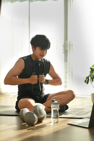 Portrait of happy young man sitting on yoga on yoga mat and exercising in living room.