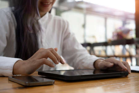 Cropped of smiling businesswoman using digital tablet on wooden desk in office.