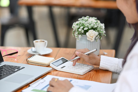 Cropped shot of female accountant analyzing business data and using calculator on office desk.