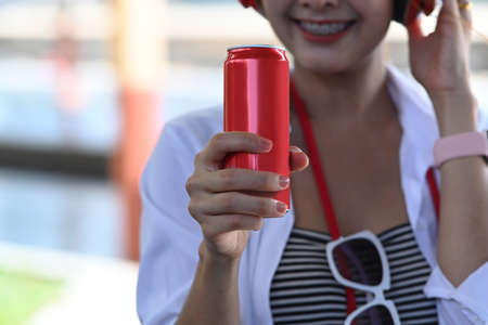 Cheerful young asian woman holding and showing mock up smart phone with blank screen.