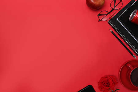 Top view stylish workplace with notebook, glasses, coffee cup, mobile phone and pen on red background.の写真素材