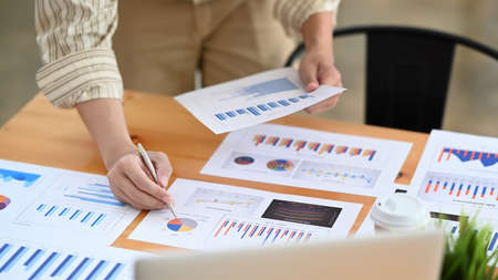 Cropped shot businesswoman analyzing financial data on wooden office desk.の写真素材
