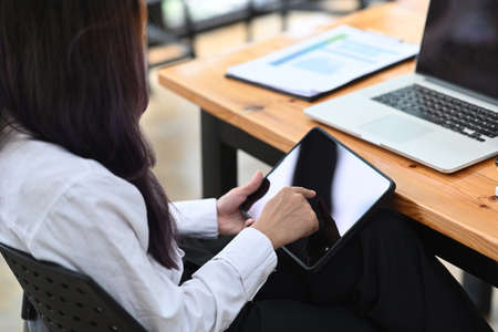 Smiling young woman holding pen and looking at laptop screen while sitting in office.の写真素材