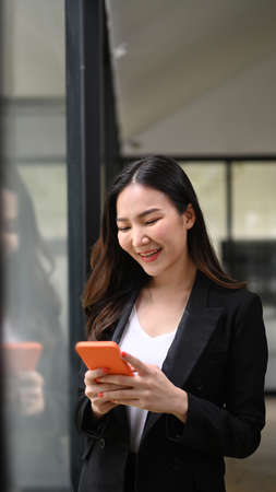 Portrait of happy businesswoman using smart phone while standing in office.の写真素材