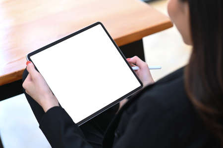 Cropped shot of businesswoman in suit reading news on digital tablet at office room.