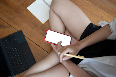 Young asian woman making note on notebook and using digital tablet while sitting on floor.