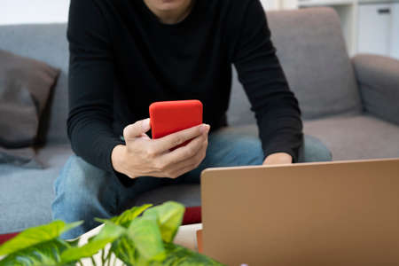 Cropped shot of young man holding coffee cup and using mobile phone at home.の写真素材
