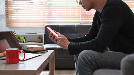 Side view young man using mobile phone on sofa.