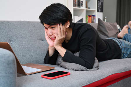 Young man playing guitar on sofa.