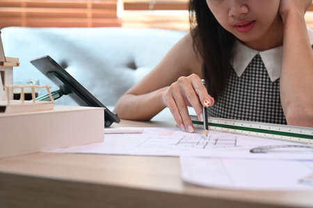 Architect woman working with computer tablet and blueprint in living room.
