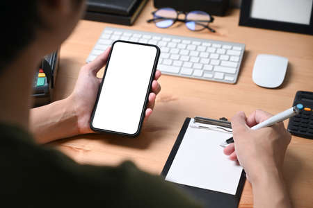 Young man using mobile phone and laptop while lying on couch.