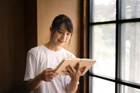 Portrait of peaceful young woman reading book in library.の写真素材
