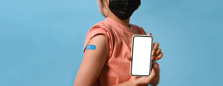 Woman in face mask holding mobile phone and showing arm after vaccination.の写真素材