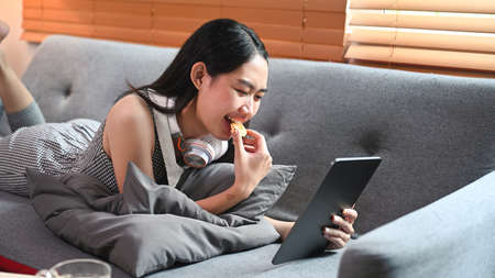 Young woman sitting on sofa and using digital tablet for surfing internet.の写真素材