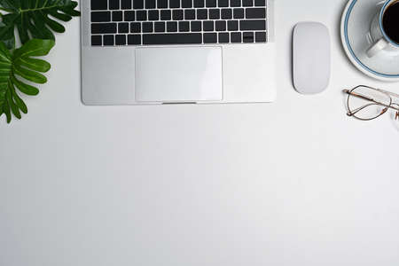 Overhead shot laptop computer, coffee cup and notebook on white office desk.