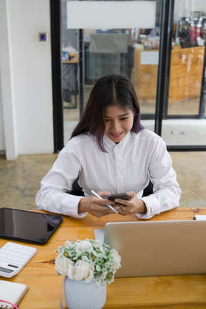 Female office worker using mobile phone at office desk.の写真素材