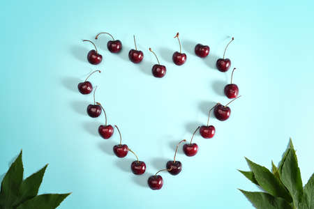 Woman hand picking up fresh cherry on pink background.