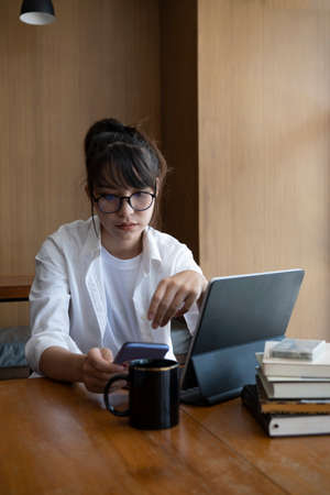 Young woman sitting in library and doing homework with computer tablet.