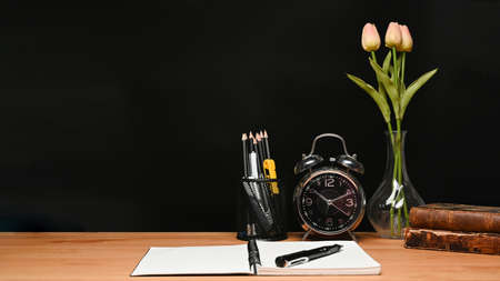 Alarm clock, pencil holder and notebook on wooden table.