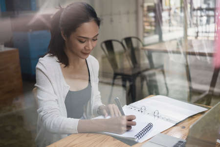 View through glass window of young woman working in modern coffee shop.の写真素材