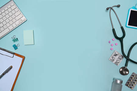 Stethoscope, clipboard and pills on blue background. Doctor workspace.