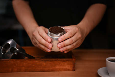 Barista holding moka pot with  ground coffee in dark room.の写真素材
