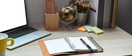 Notebook, laptop computer and supplies on wooden desk.