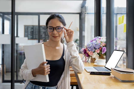 Confident creative designer woman in eyeglasses sitting in modern workplace and smiling to camera.の写真素材
