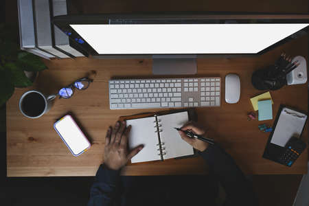 Overhead shot man making note on notebook and working with computer.の写真素材