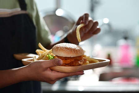 Woman holding tray of homemade burgers with fried potatoes and glass of soft drink.