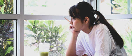 Peaceful young female student sitting in cafe and looking out of window.