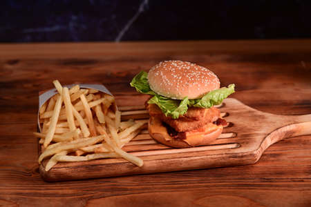 Homemade hamburger and fried potatoes on wooden tray.