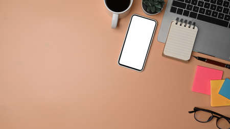 Top view mock up mobile phone, laptop computer and notebook on white desk.