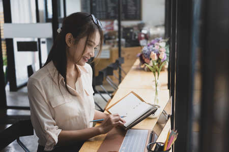 Attractive young woman sitting in coffee shop and working with laptop computer.の写真素材