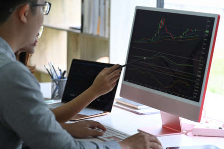 Businessman working with charts and market reports on computer screens.