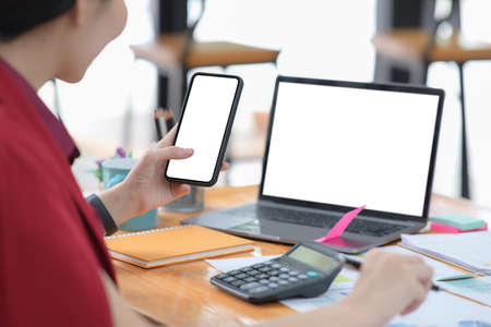Businesswoman using mobile phone and working with laptop computer at office.